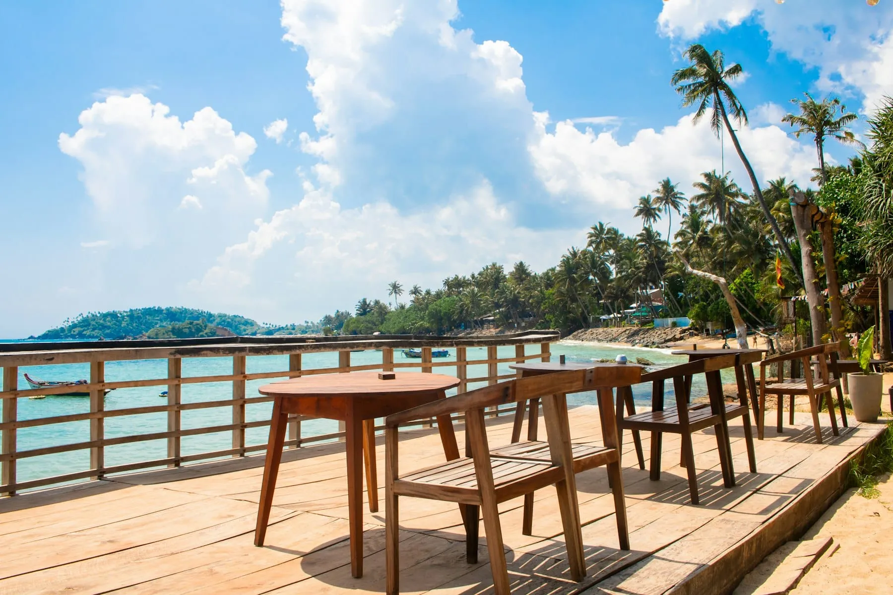 Een houten terras met tafels en stoelen aan het strand