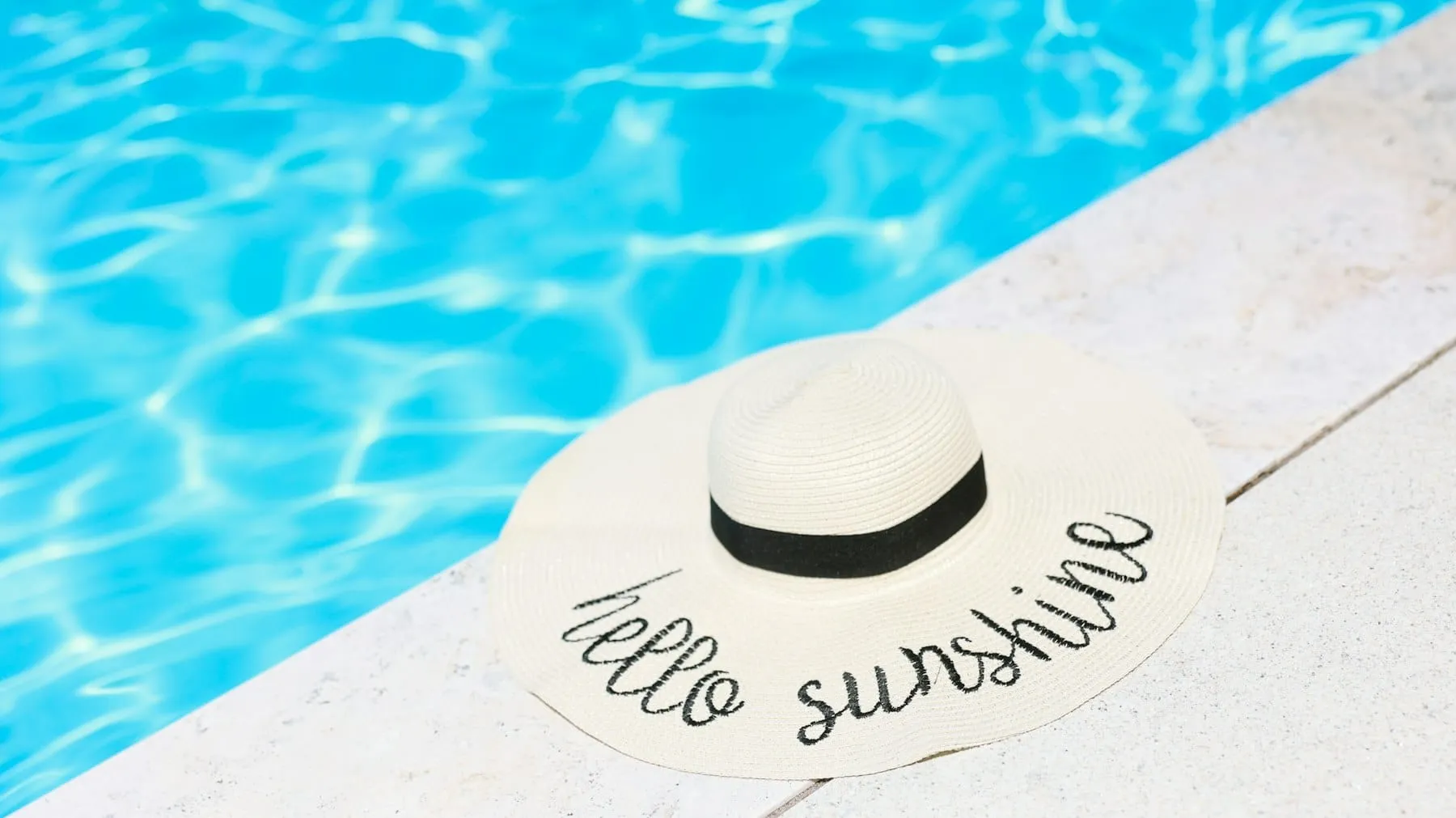 A guest in a white sun hat sitting at the edge of a resort pool