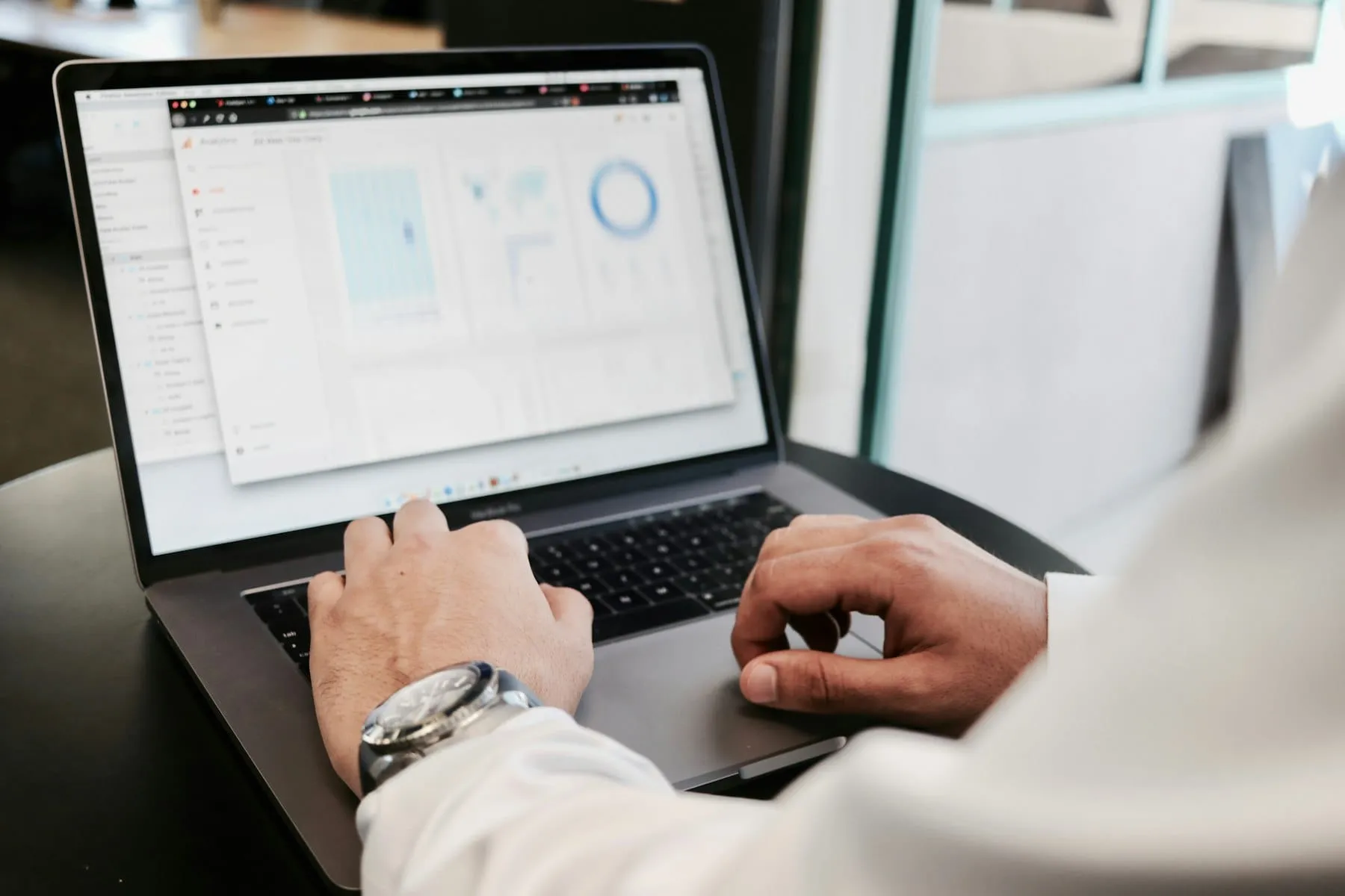 Hands typing on a laptop that shows charts, with glasses and a phone beside it