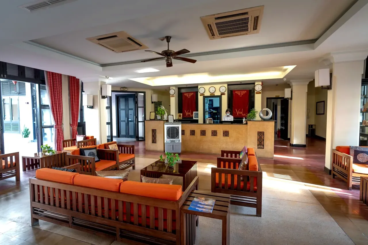 Een hotellobby met houten meubels, oranje kussens en een receptie