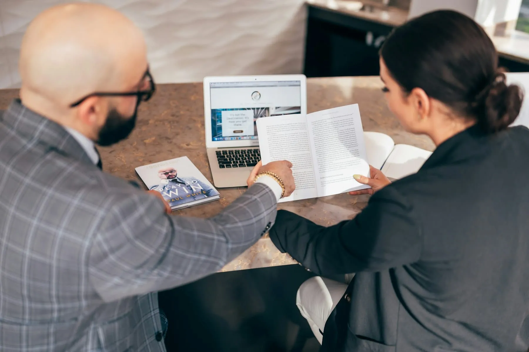 Two colleagues leaning over a table to review printed work together