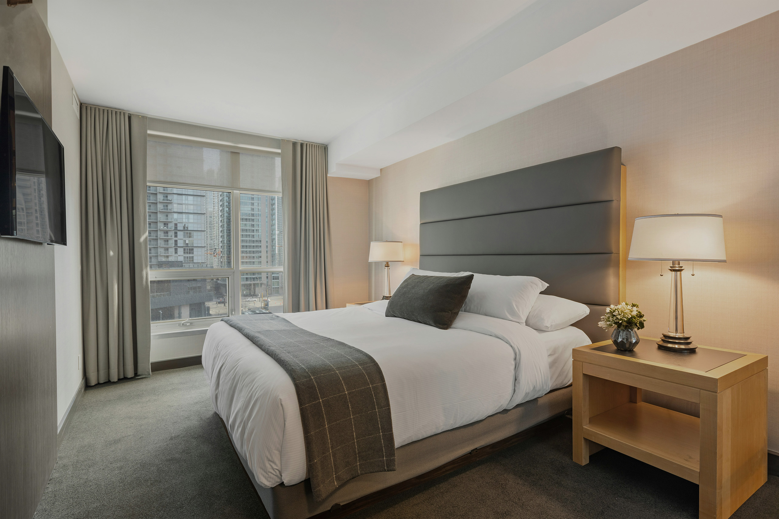 Een lichte hotelkamer met een opgemaakt bed, een leeslamp en hoge ramen
